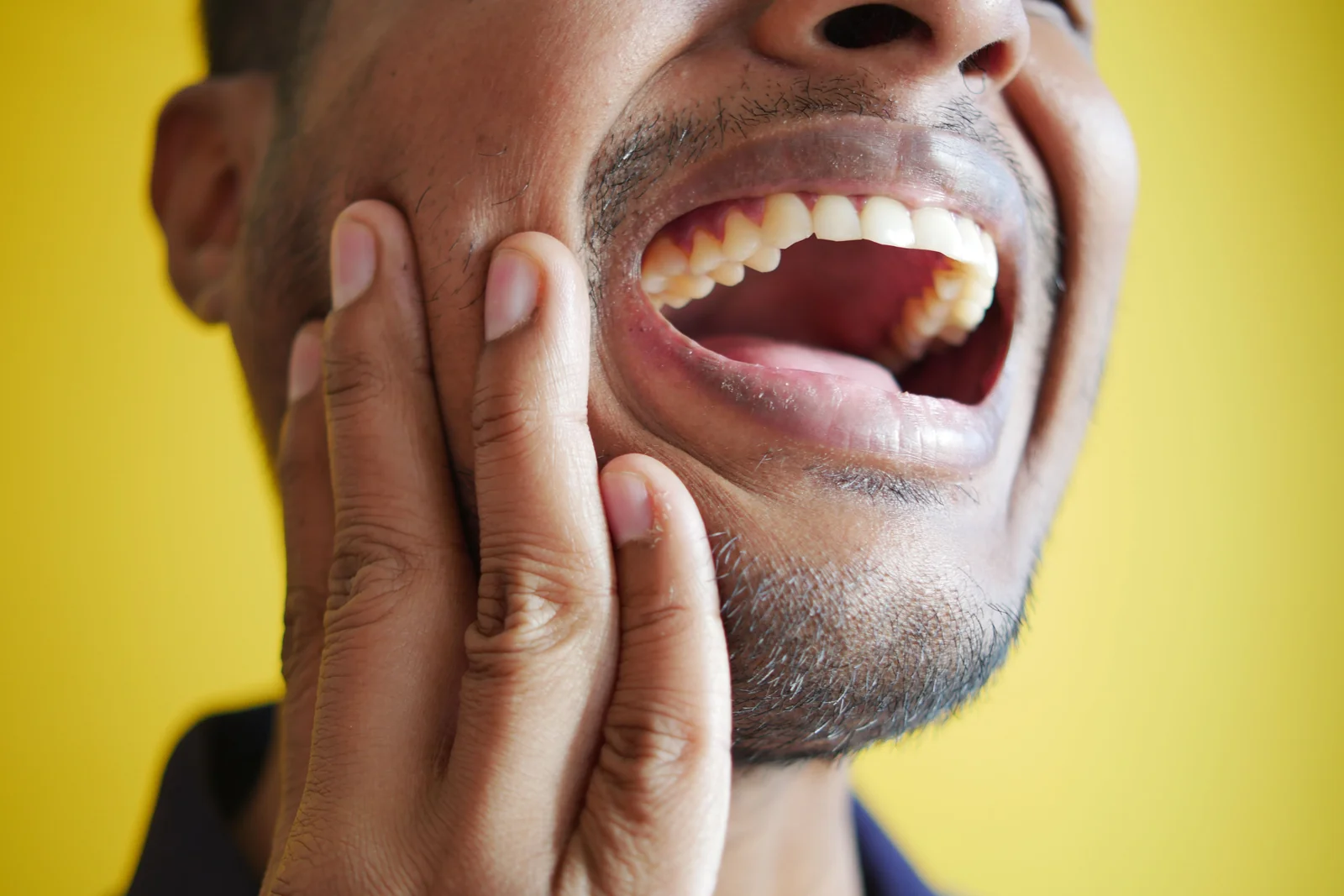 Homem com a boca aberta levando a mao a mandibula por dor