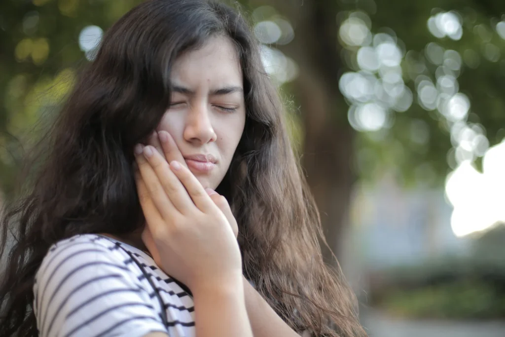 Mulher ao ar livre com a mao sobre a mandibula demonstrando dor