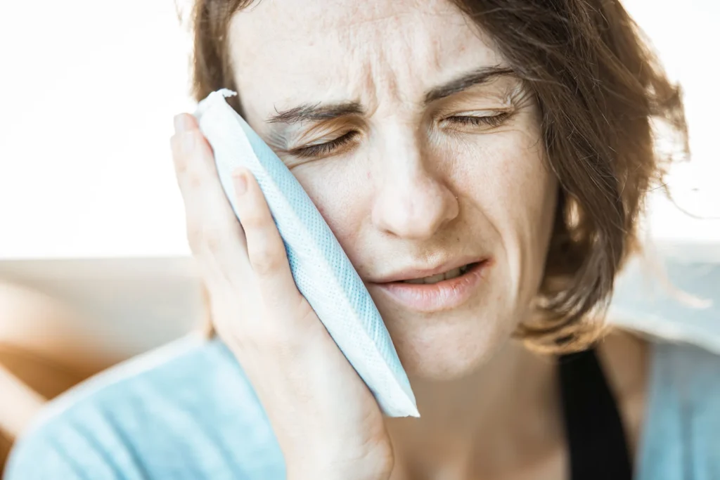 Mulher com dor facial aplicando compressa fria na regiao da mandibula